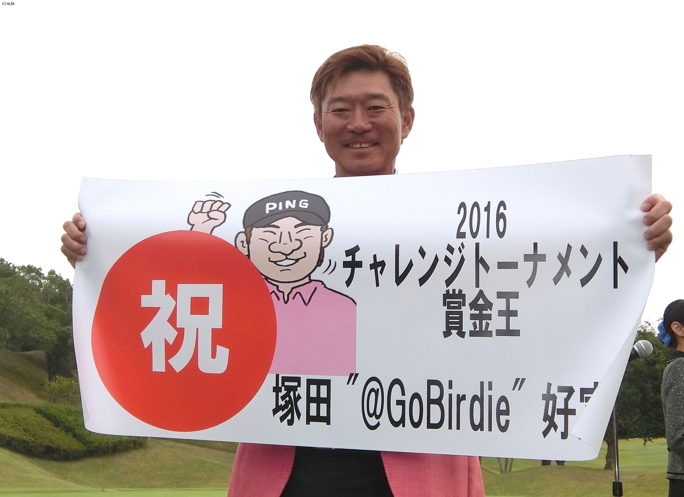 似顔絵入りの横断幕を手に笑顔を見せる塚田好宣（撮影：赤澤亮丈）